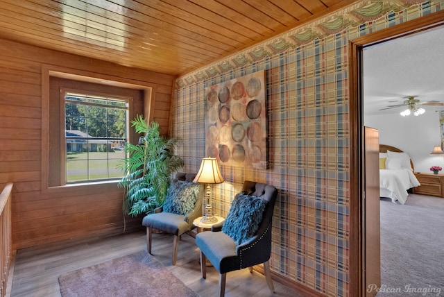 sitting room featuring wood walls, ceiling fan, light hardwood / wood-style floors, and wooden ceiling