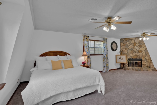 carpeted bedroom with a textured ceiling, a stone fireplace, and ceiling fan