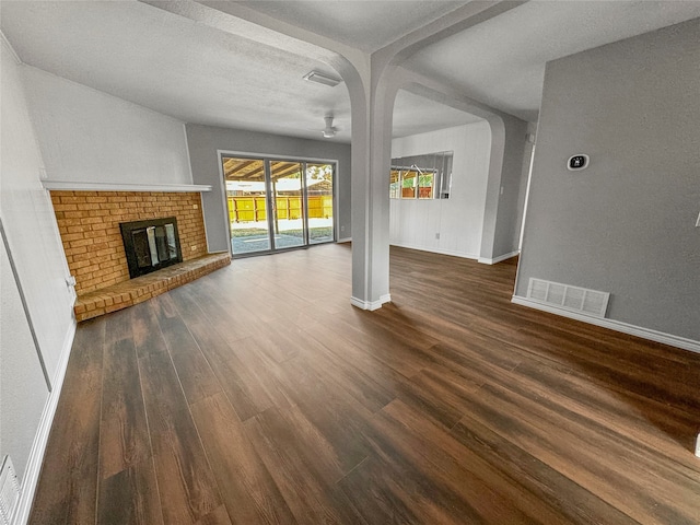 unfurnished living room featuring a brick fireplace, a textured ceiling, and dark hardwood / wood-style flooring