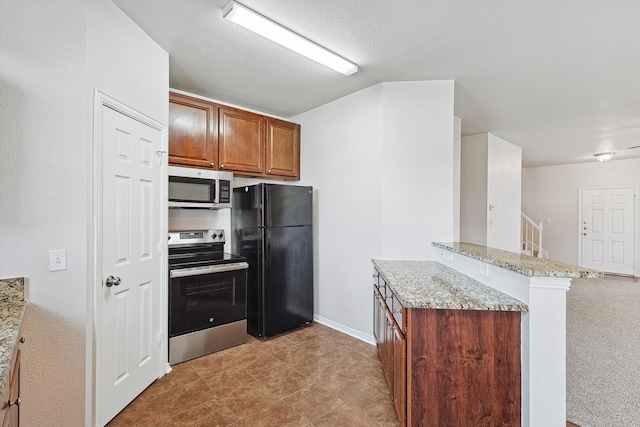 kitchen featuring light stone counters, kitchen peninsula, a textured ceiling, appliances with stainless steel finishes, and light colored carpet