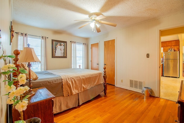 bedroom with stainless steel fridge, light wood-type flooring, ceiling fan, and a textured ceiling