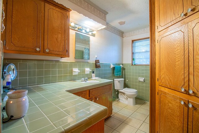 bathroom featuring vanity, tile walls, crown molding, toilet, and a textured ceiling