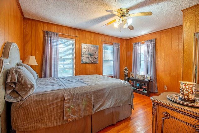 bedroom featuring wood walls, light hardwood / wood-style floors, a textured ceiling, and ceiling fan