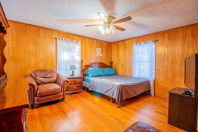 bedroom featuring a textured ceiling, ceiling fan, wood walls, and light hardwood / wood-style flooring