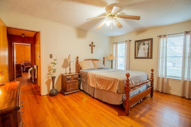 bedroom featuring ceiling fan, a textured ceiling, light wood-type flooring, and multiple windows