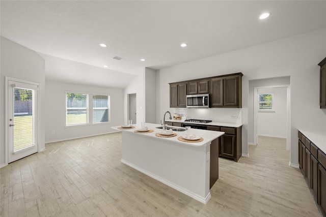 kitchen featuring lofted ceiling, an island with sink, sink, dark brown cabinetry, and light hardwood / wood-style floors