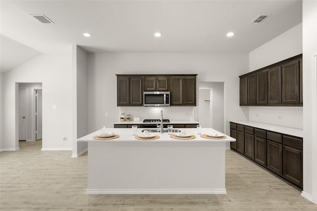 kitchen with light hardwood / wood-style flooring, dark brown cabinets, sink, and an island with sink