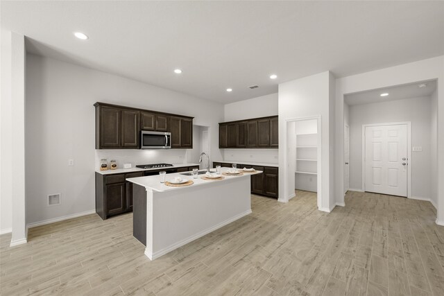 kitchen with appliances with stainless steel finishes, sink, an island with sink, light hardwood / wood-style floors, and dark brown cabinetry