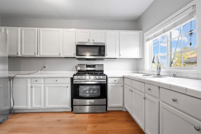 kitchen with stainless steel appliances, light hardwood / wood-style floors, white cabinets, and tile countertops