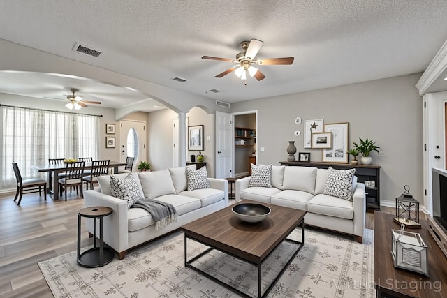 living room featuring light wood finished floors, visible vents, arched walkways, ceiling fan, and ornate columns