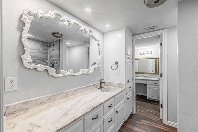 full bath featuring a textured ceiling, visible vents, wood finished floors, tiled shower, and vanity