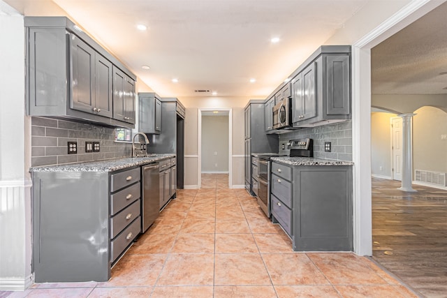 kitchen with appliances with stainless steel finishes, decorative columns, gray cabinets, and light stone counters