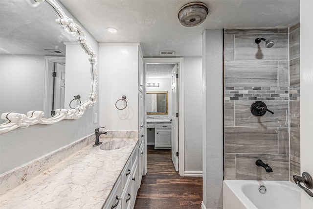full bath featuring a textured ceiling, visible vents, wood finished floors, vanity, and bathing tub / shower combination