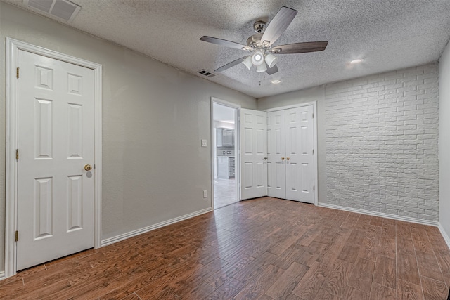 unfurnished bedroom with ceiling fan, brick wall, wood-type flooring, and a textured ceiling