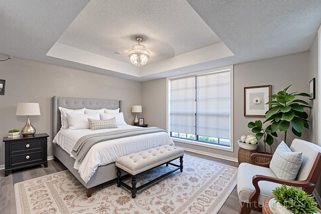 bedroom with a raised ceiling, a textured ceiling, and wood finished floors