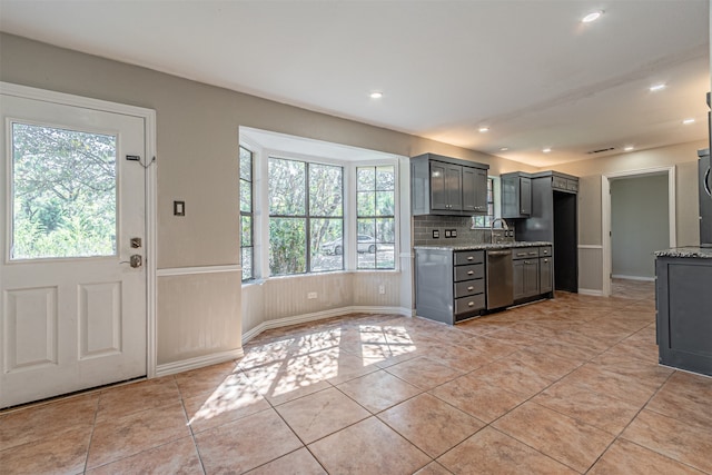 kitchen with light stone counters, stainless steel dishwasher, gray cabinetry, light tile patterned floors, and backsplash