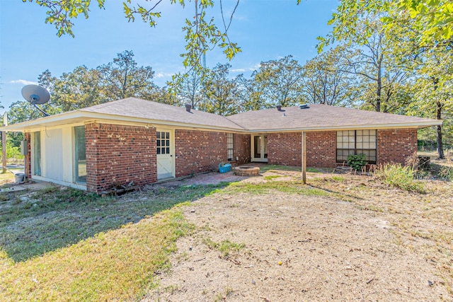 back of house with brick siding, an outdoor fire pit, and a yard