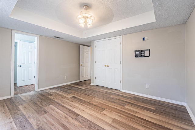 unfurnished bedroom featuring ceiling fan, hardwood / wood-style floors, a closet, a tray ceiling, and a textured ceiling