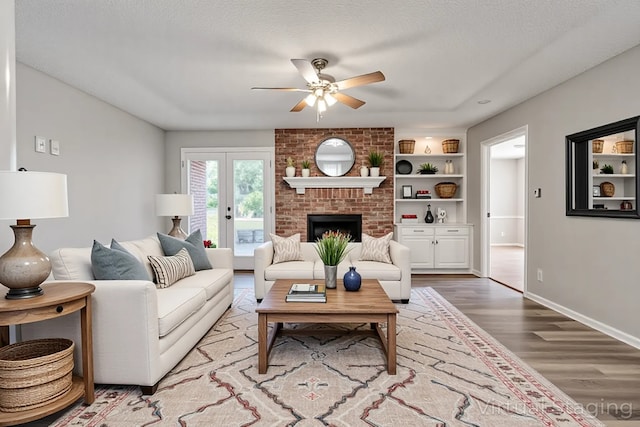 living area with a ceiling fan, wood finished floors, a textured ceiling, a brick fireplace, and baseboards