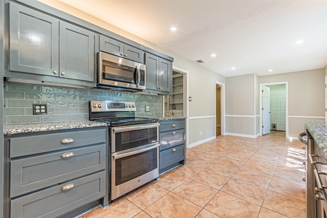 kitchen featuring light stone countertops, appliances with stainless steel finishes, light tile patterned floors, visible vents, and decorative backsplash