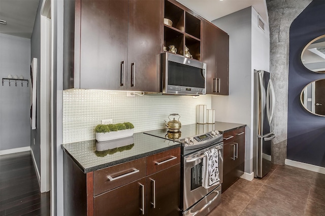 kitchen with dark tile patterned floors, dark brown cabinets, backsplash, appliances with stainless steel finishes, and dark stone countertops