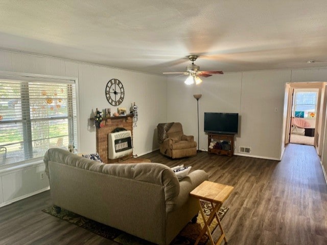 living room with ceiling fan, heating unit, dark wood-type flooring, and a healthy amount of sunlight