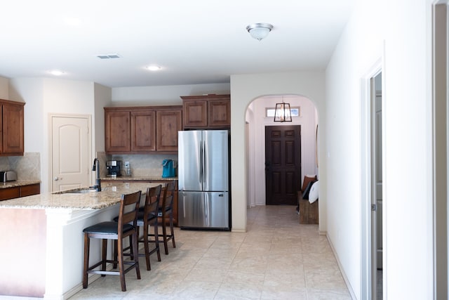 kitchen with stainless steel refrigerator, sink, a center island with sink, a kitchen bar, and backsplash