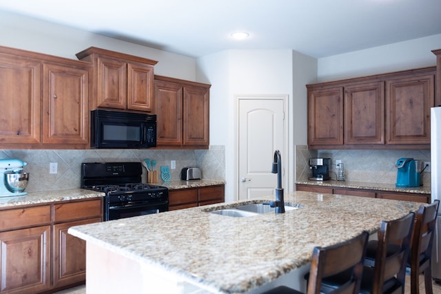 kitchen with a breakfast bar area, black appliances, sink, and a kitchen island with sink