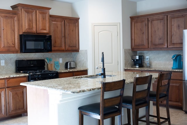 kitchen featuring tasteful backsplash, an island with sink, black appliances, and light stone counters