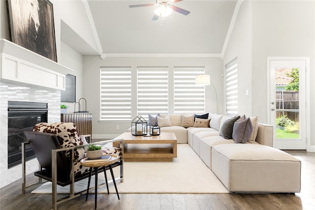 living room featuring ceiling fan, a tiled fireplace, crown molding, hardwood / wood-style floors, and high vaulted ceiling