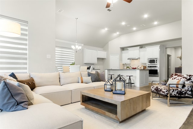 living room featuring ceiling fan with notable chandelier, high vaulted ceiling, light hardwood / wood-style flooring, and sink