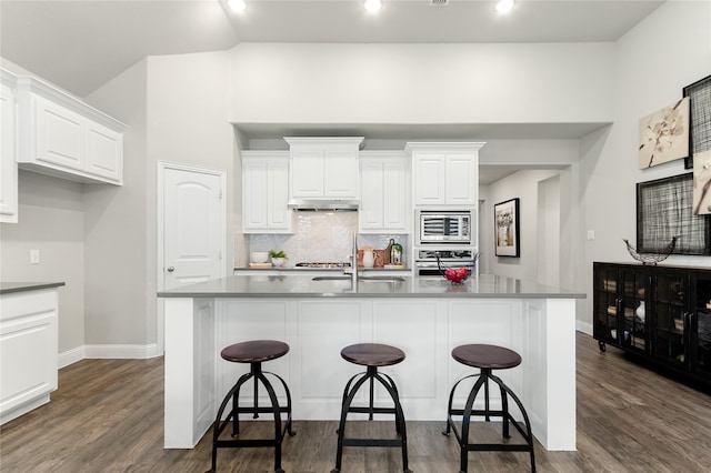 kitchen featuring a center island with sink, stainless steel appliances, dark hardwood / wood-style floors, a kitchen bar, and white cabinetry