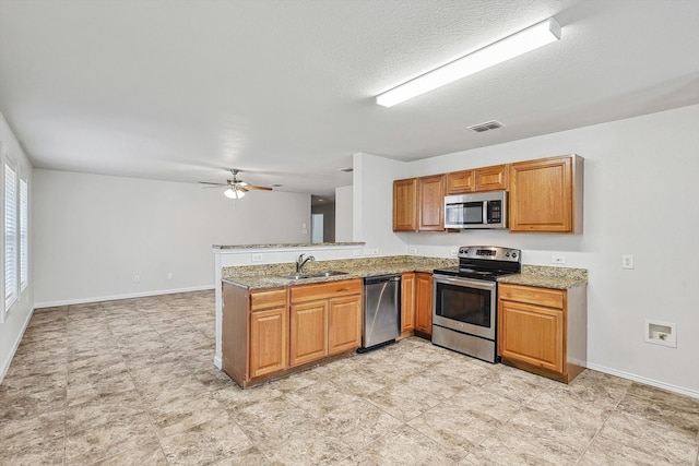 kitchen with light stone counters, ceiling fan, sink, kitchen peninsula, and appliances with stainless steel finishes