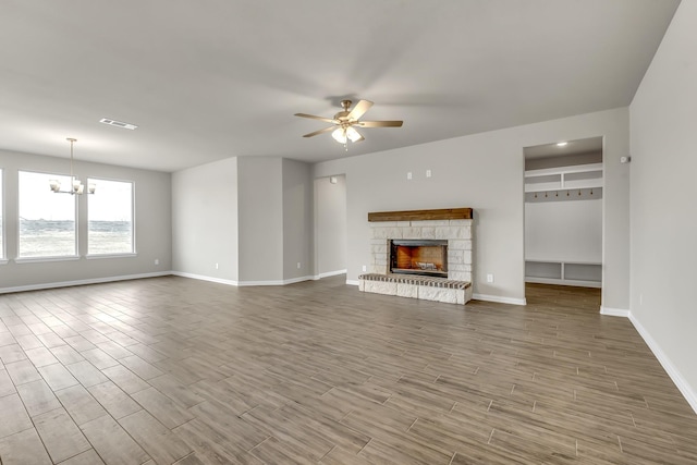 unfurnished living room featuring ceiling fan with notable chandelier and a stone fireplace