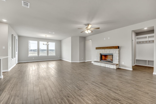 unfurnished living room with ceiling fan with notable chandelier and a stone fireplace