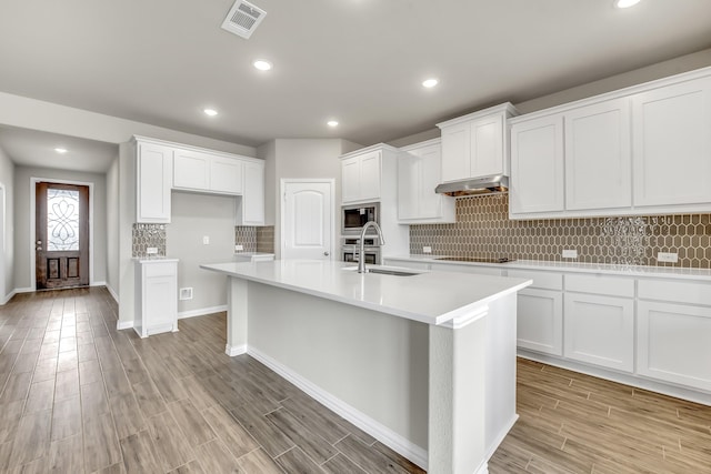 kitchen featuring sink, an island with sink, white cabinets, and built in microwave