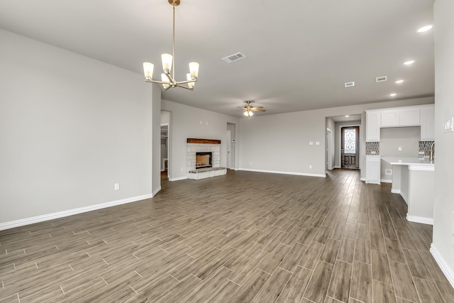 unfurnished living room with ceiling fan with notable chandelier and a stone fireplace