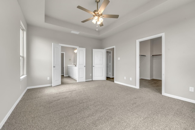 unfurnished bedroom with a walk in closet, carpet floors, connected bathroom, ceiling fan, and a tray ceiling