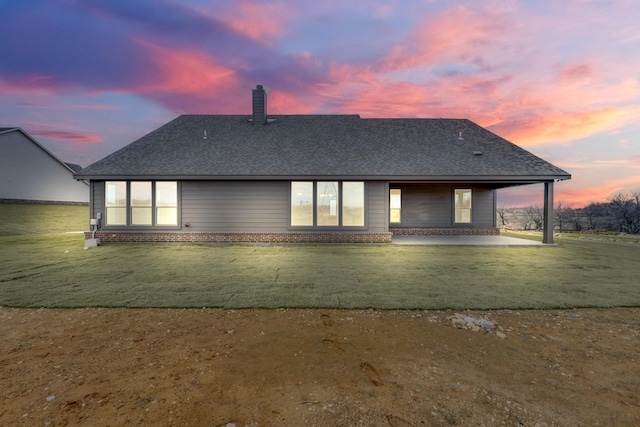 back house at dusk with a lawn and a patio