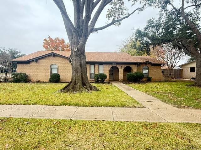 ranch-style home with a front yard, brick siding, and fence