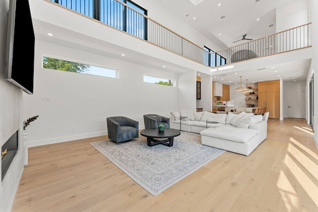 living room featuring ceiling fan, light hardwood / wood-style flooring, a towering ceiling, and a large fireplace