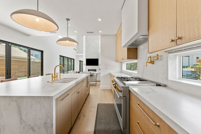 kitchen with an island with sink, wall chimney range hood, high end stainless steel range, and decorative light fixtures