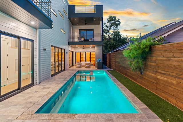 pool at dusk with outdoor lounge area and a patio