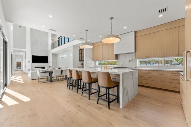 kitchen featuring hanging light fixtures, a large island, light hardwood / wood-style flooring, a large fireplace, and a kitchen bar