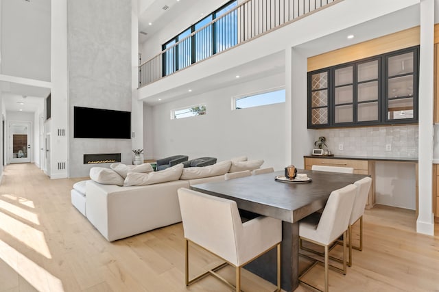 dining space featuring a towering ceiling, light hardwood / wood-style floors, and a fireplace