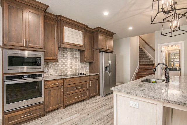 kitchen with stainless steel appliances, tasteful backsplash, sink, hanging light fixtures, and light hardwood / wood-style flooring