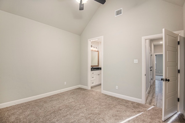 unfurnished bedroom featuring ceiling fan, light colored carpet, ensuite bathroom, and high vaulted ceiling