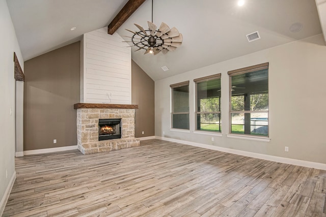 unfurnished living room with high vaulted ceiling, beam ceiling, a stone fireplace, and light hardwood / wood-style floors