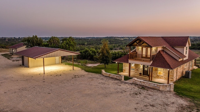 property exterior at dusk featuring central AC unit, a balcony, and a lawn