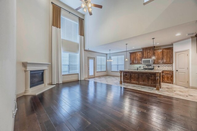 941 Lake Meadow Ln, Little Elm, TX 75068 - living room with visible vents, a towering ceiling, a glass covered fireplace, hardwood / wood-style flooring, and a ceiling fan